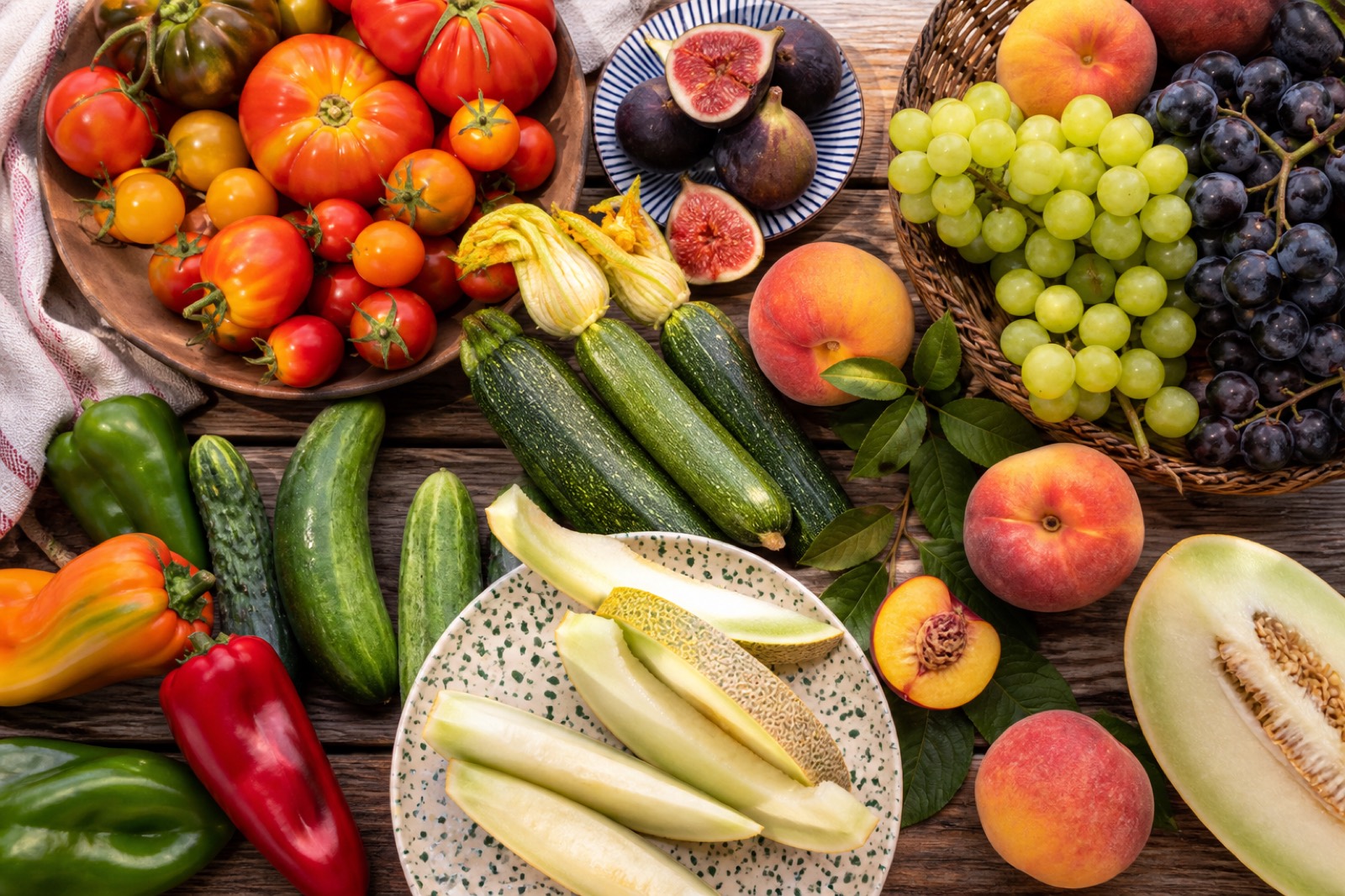 Tomates, pimentos, courgettes, pêssegos, figos, uvas e melão sobre mesa de madeira